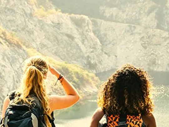 Young people on a hike, overlooking a lake surrounded by mountains.