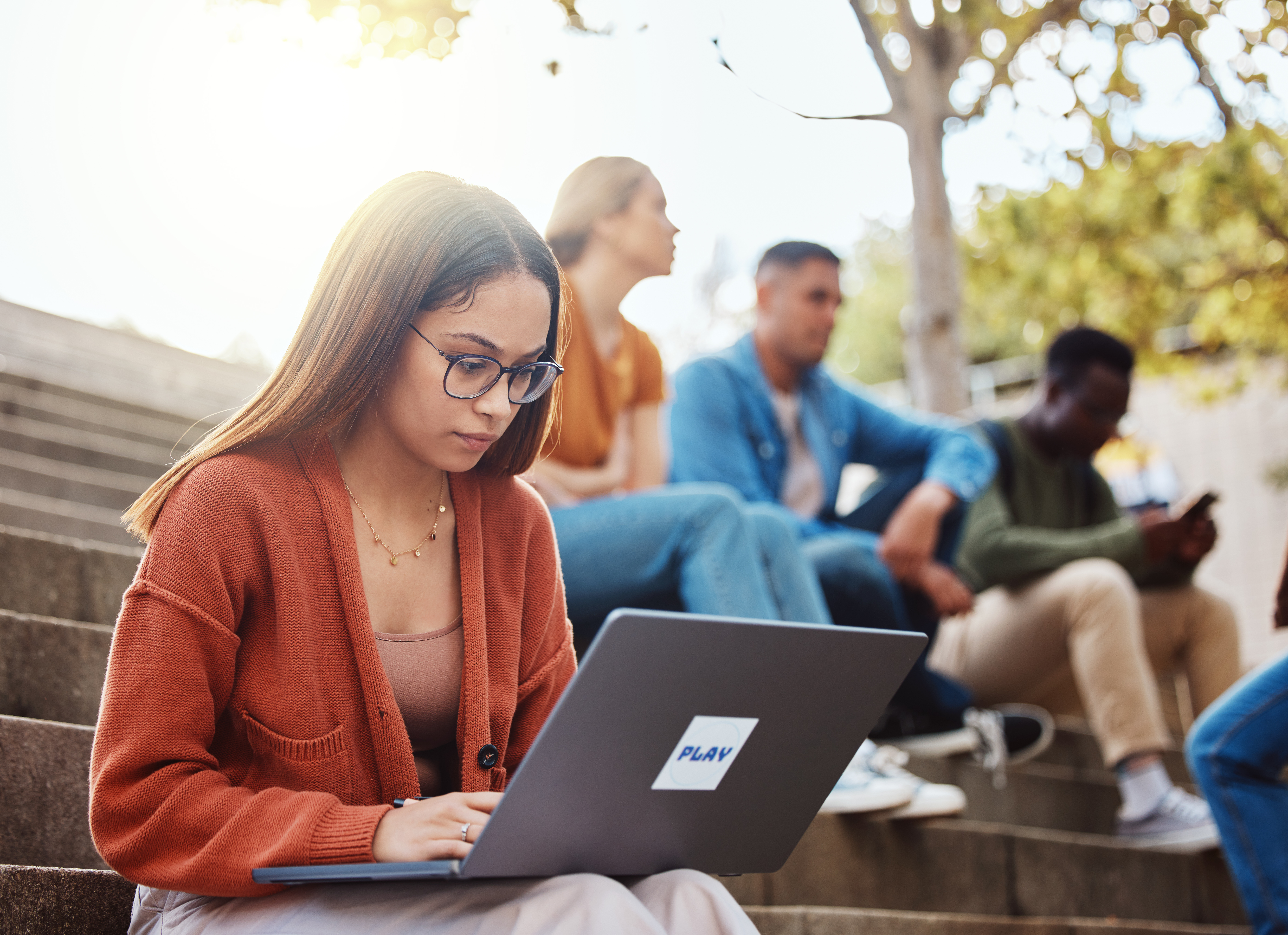 Focused female student working on a laptop outdoors in a group setting, symbolizing personalised, self-regulated learning. This represents how Pamoja Education's flexible, asynchronous delivery allows gifted students to progress at a faster pace and achieve academic excellence.