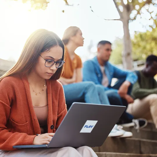 Focused female student working on a laptop outdoors in a group setting, symbolizing personalised, self-regulated learning. This represents how Pamoja Education's flexible, asynchronous delivery allows gifted students to progress at a faster pace and achieve academic excellence.
