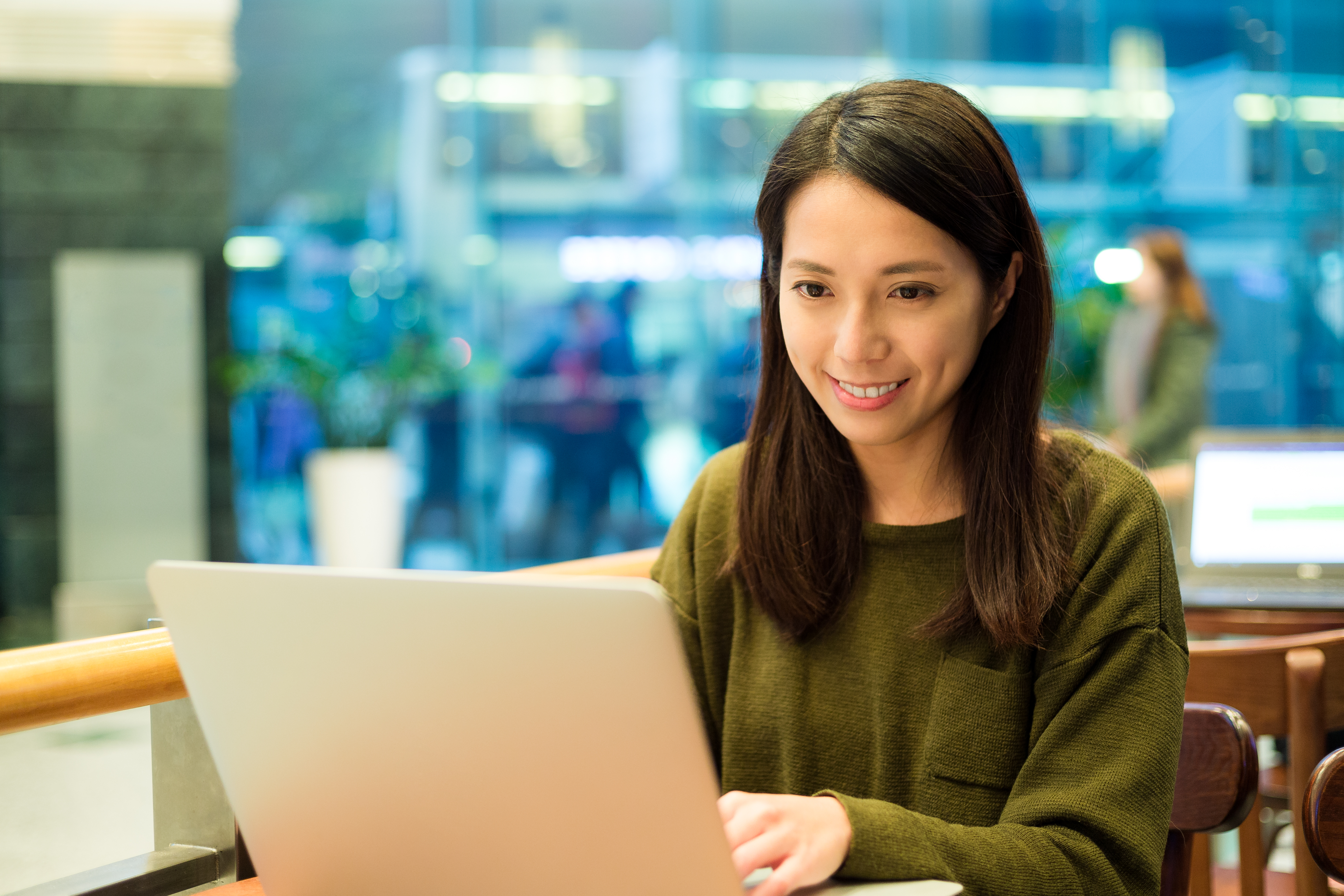A young woman with curly hair in a black blazer and striped shirt gestures with her hands while speaking to a person opposite her in a modern office, representing a focused computer science discussion or interview.