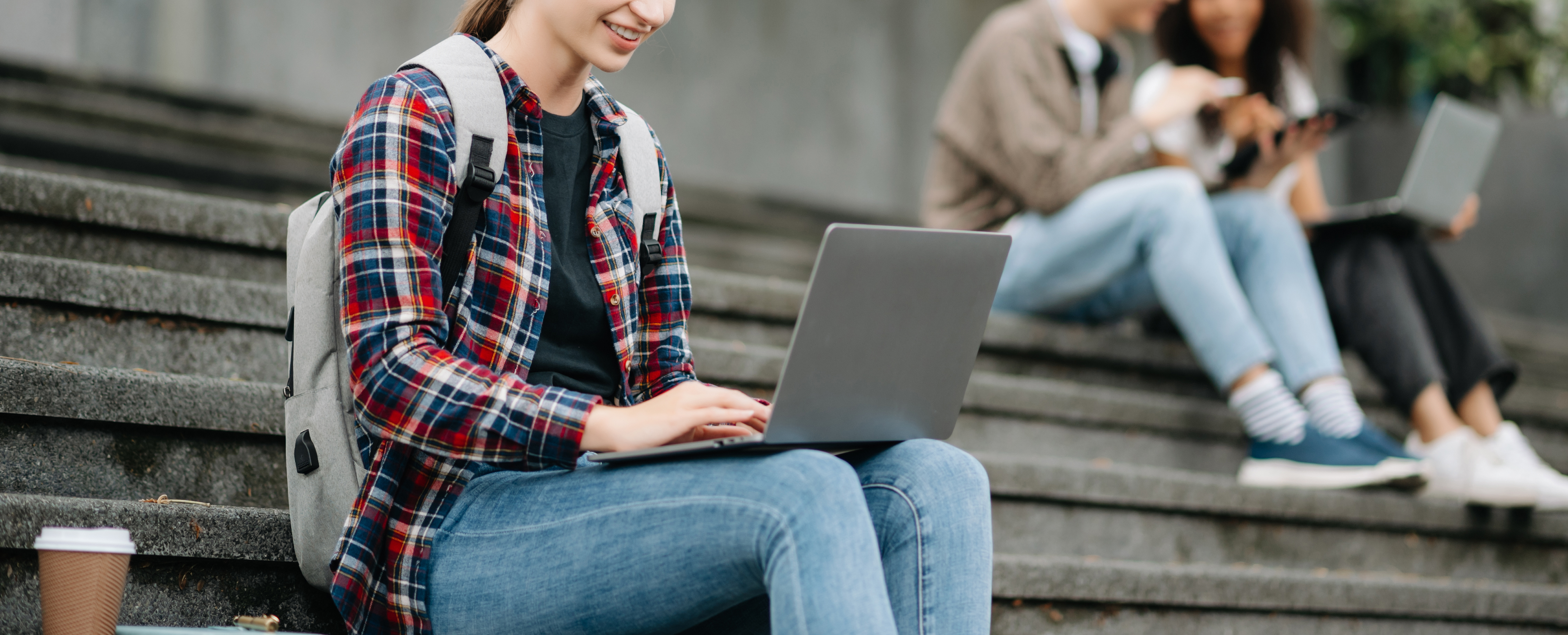 Female student with backpack using a laptop on stairs, representing digital learning and student safety at Pamoja Education.