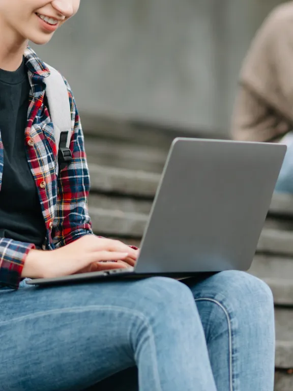 Female student with backpack using a laptop on stairs, representing digital learning and student safety at Pamoja Education.