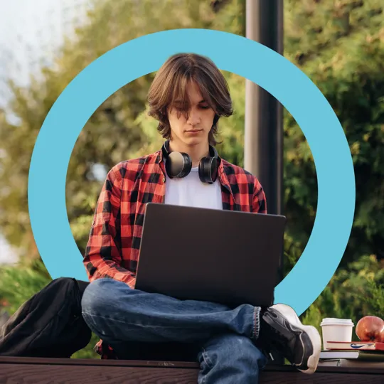 School student studying on a laptop outdoors on a bench, representing the flexibility of Pamoja's online courses.