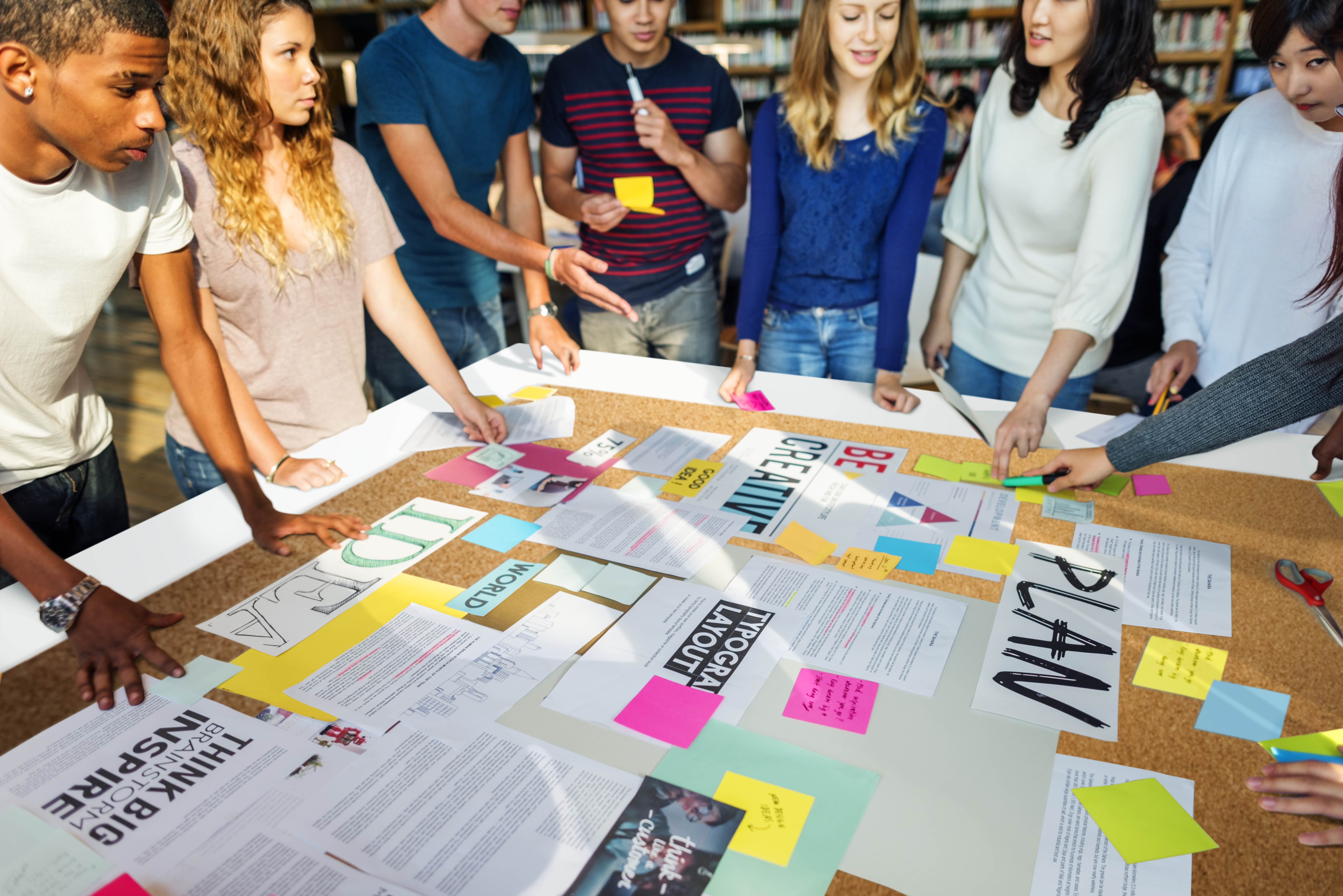 A diverse group of college students collaborating on a project, gathering around a table covered with papers, plans, and sticky notes.
