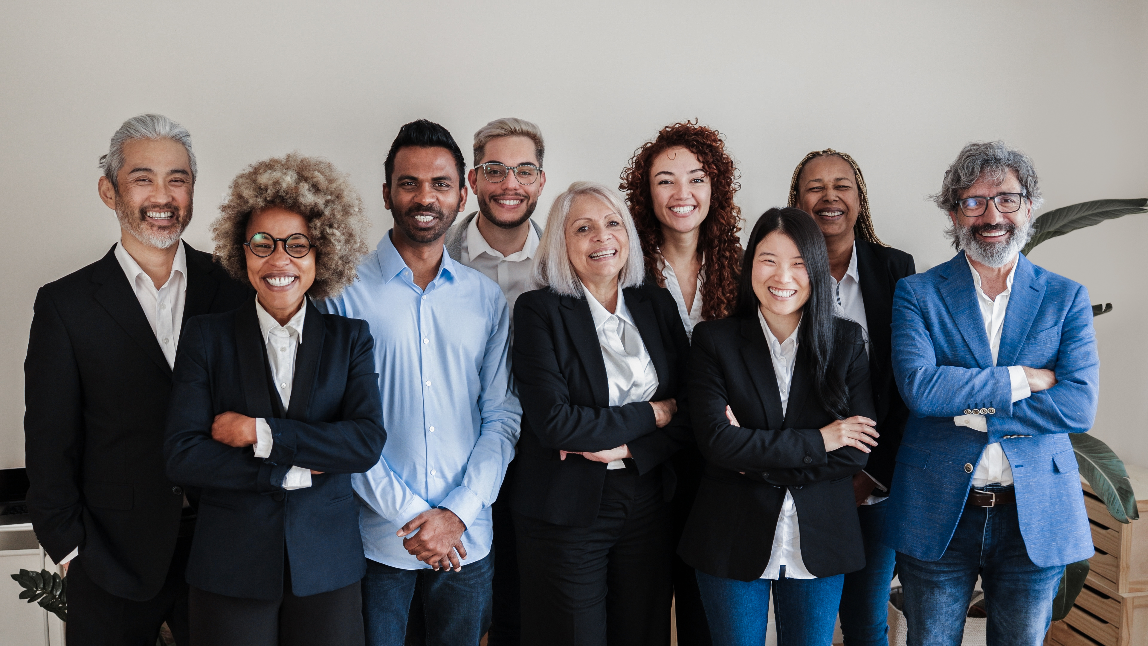 A professional group portrait of a diverse academic team, consisting of nine smiling adults, standing in an office setting.