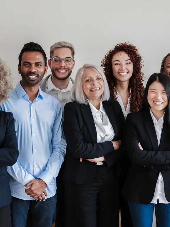A professional group portrait of a diverse academic team, consisting of nine smiling adults, standing in an office setting.