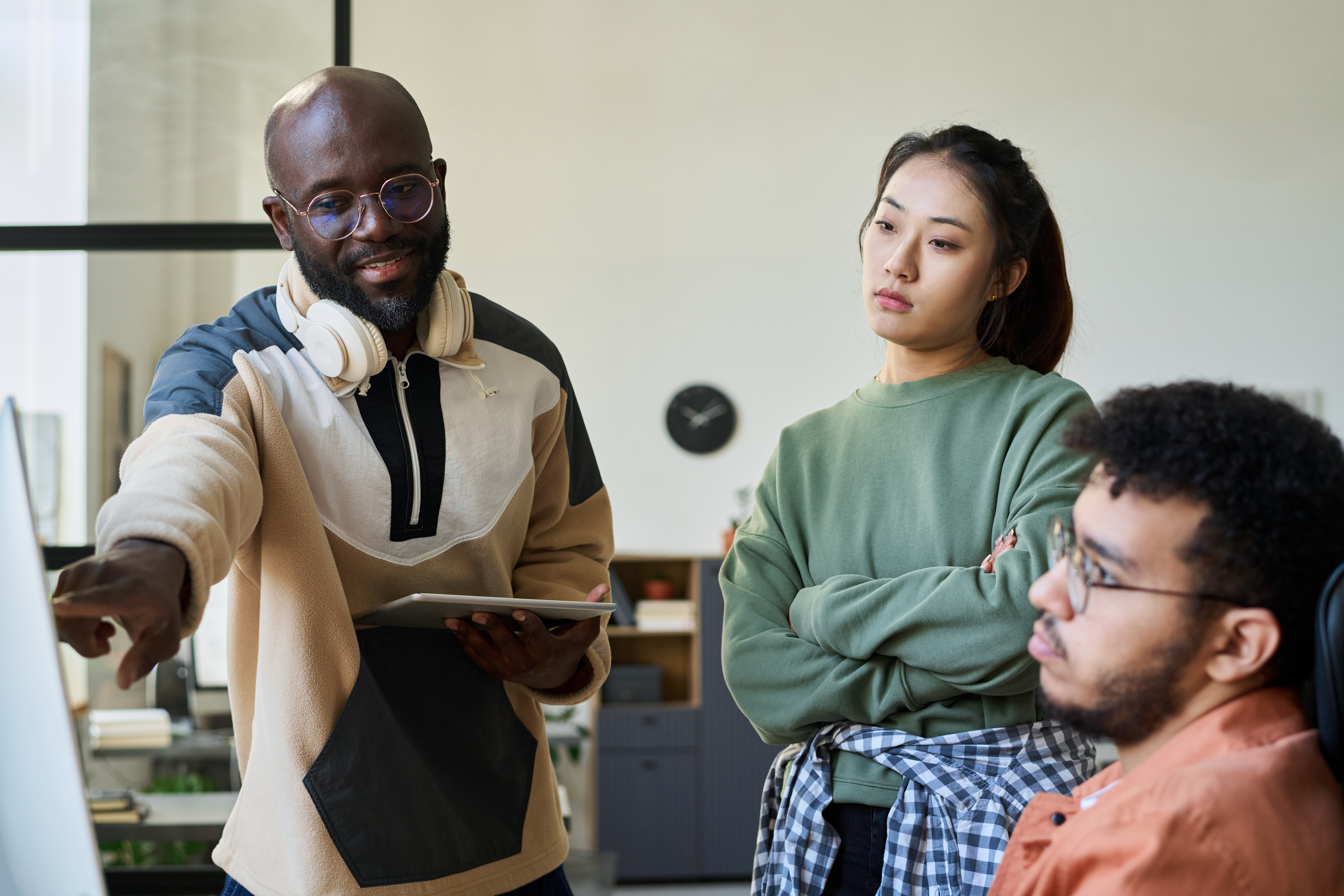 Two students, a young woman in a yellow sweater and a young man in a green sweatshirt, collaborate on a whiteboard with markers in a bright classroom.