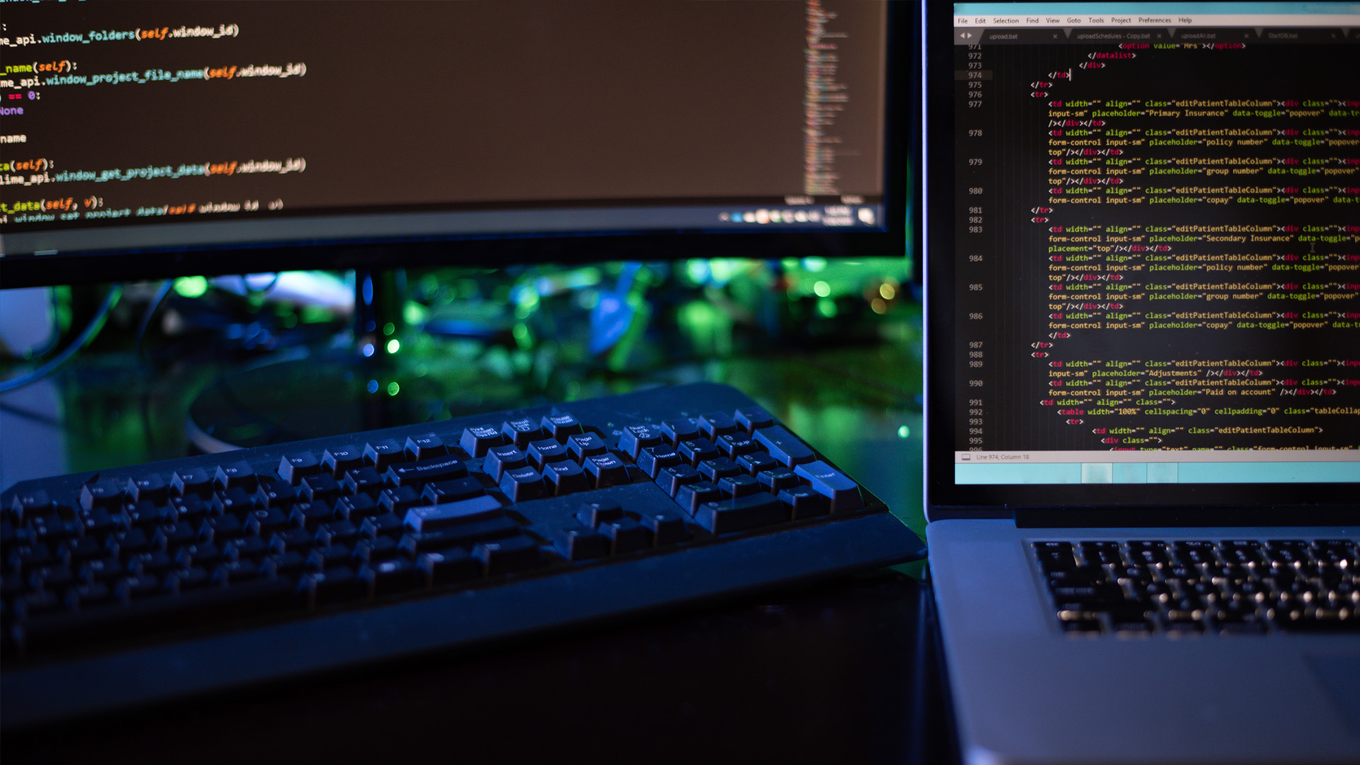 A young woman in a green sweater and glasses smiles while focused on working on a silver laptop in a brightly lit, modern indoor public area.