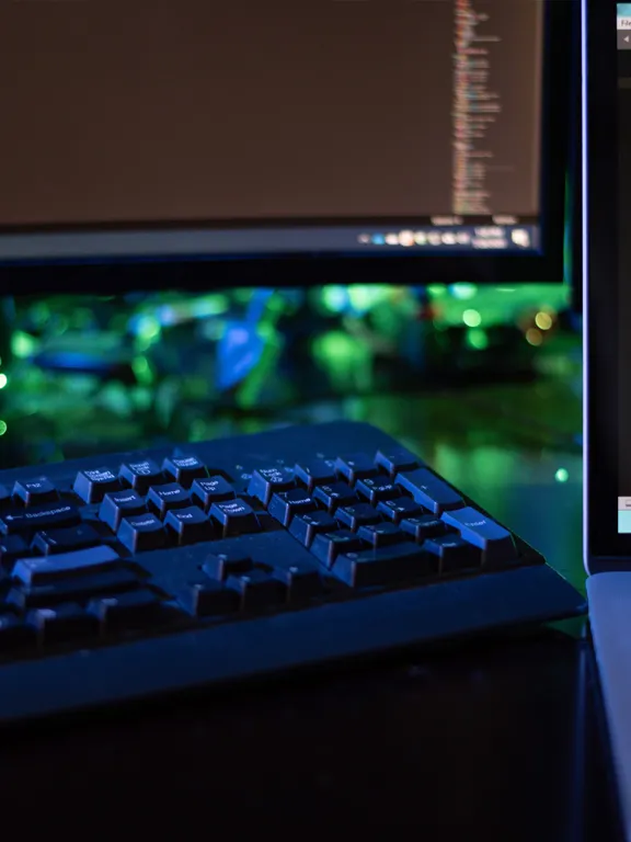 A young woman in a green sweater and glasses smiles while focused on working on a silver laptop in a brightly lit, modern indoor public area.