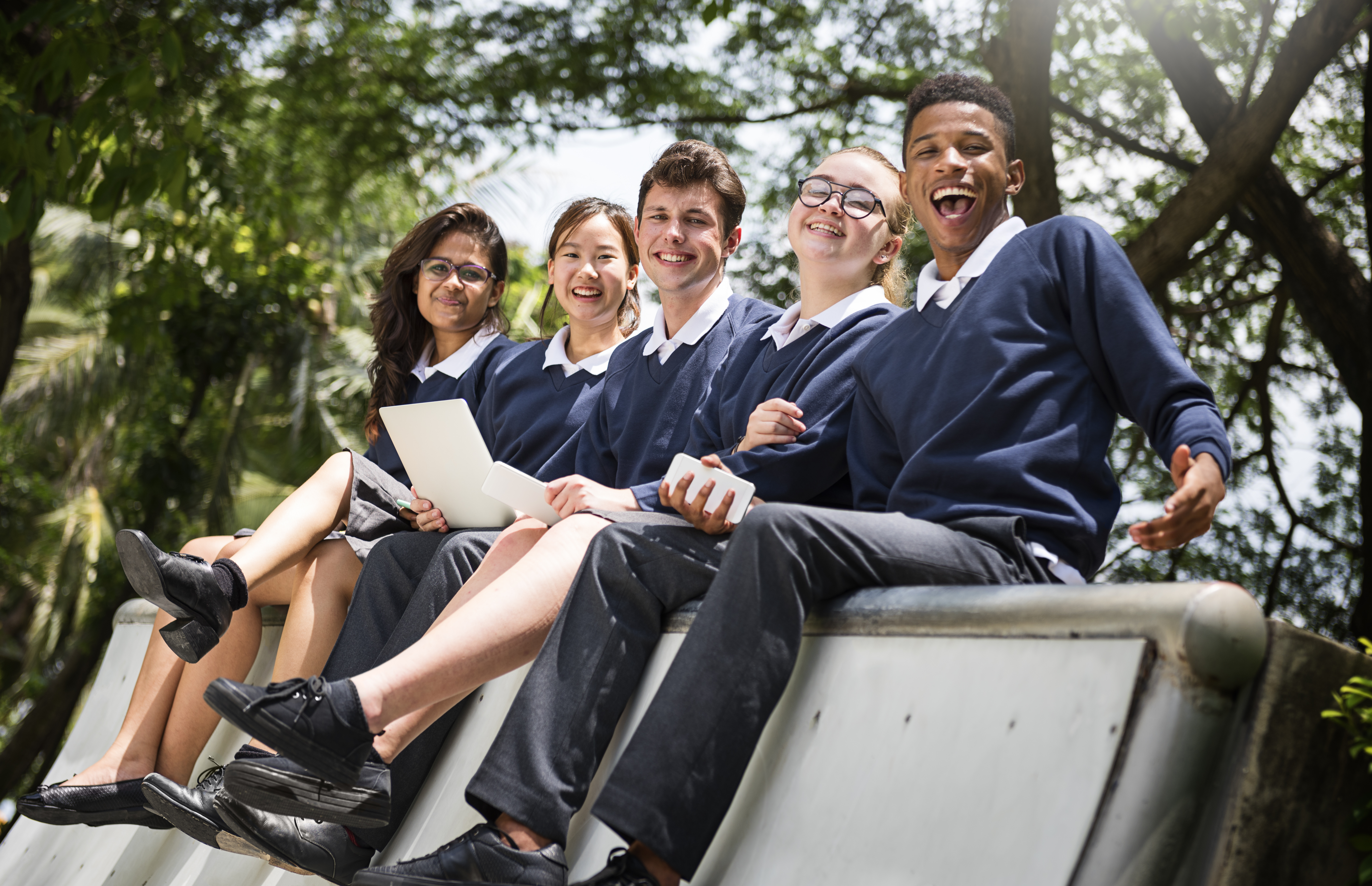Group of diverse, happy students in school uniforms sitting outside, representing the thriving community in Pamoja's developing IB Schools.