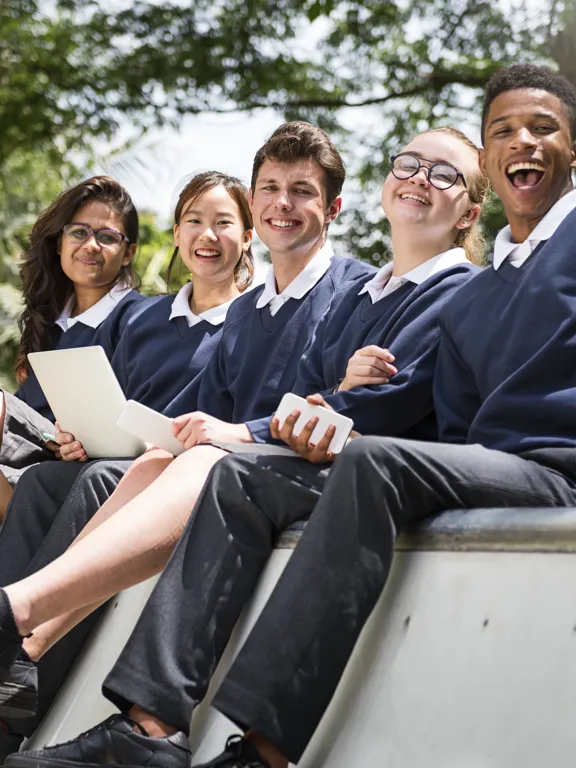 Group of diverse, happy students in school uniforms sitting outside, representing the thriving community in Pamoja's developing IB Schools.