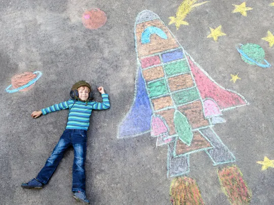 Young child laid down next to colourful chalk art.