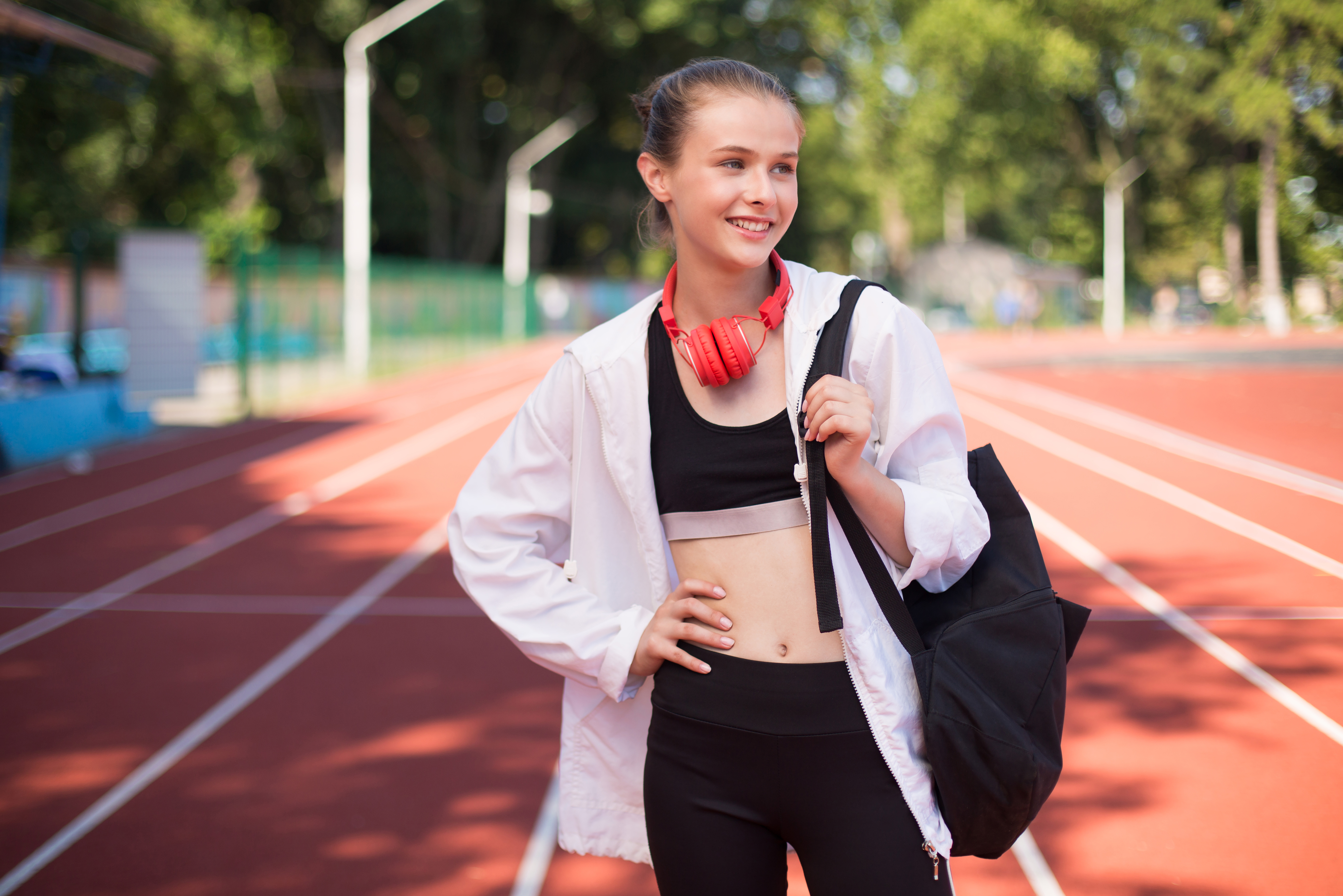 Smiling elite student-athlete standing on a running track with a sports bag and headphones. This represents the flexibility of online learning that empowers elite performers and athletes to manage rigorous training and competition schedules while achieving academic success.