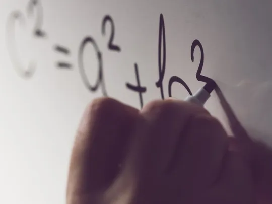 Close-up shot of a hand writing a mathematical equation, c 2 =a 2 +b 2 , on a white board with a black marker. The equation is a representation of the Pythagorean theorem.