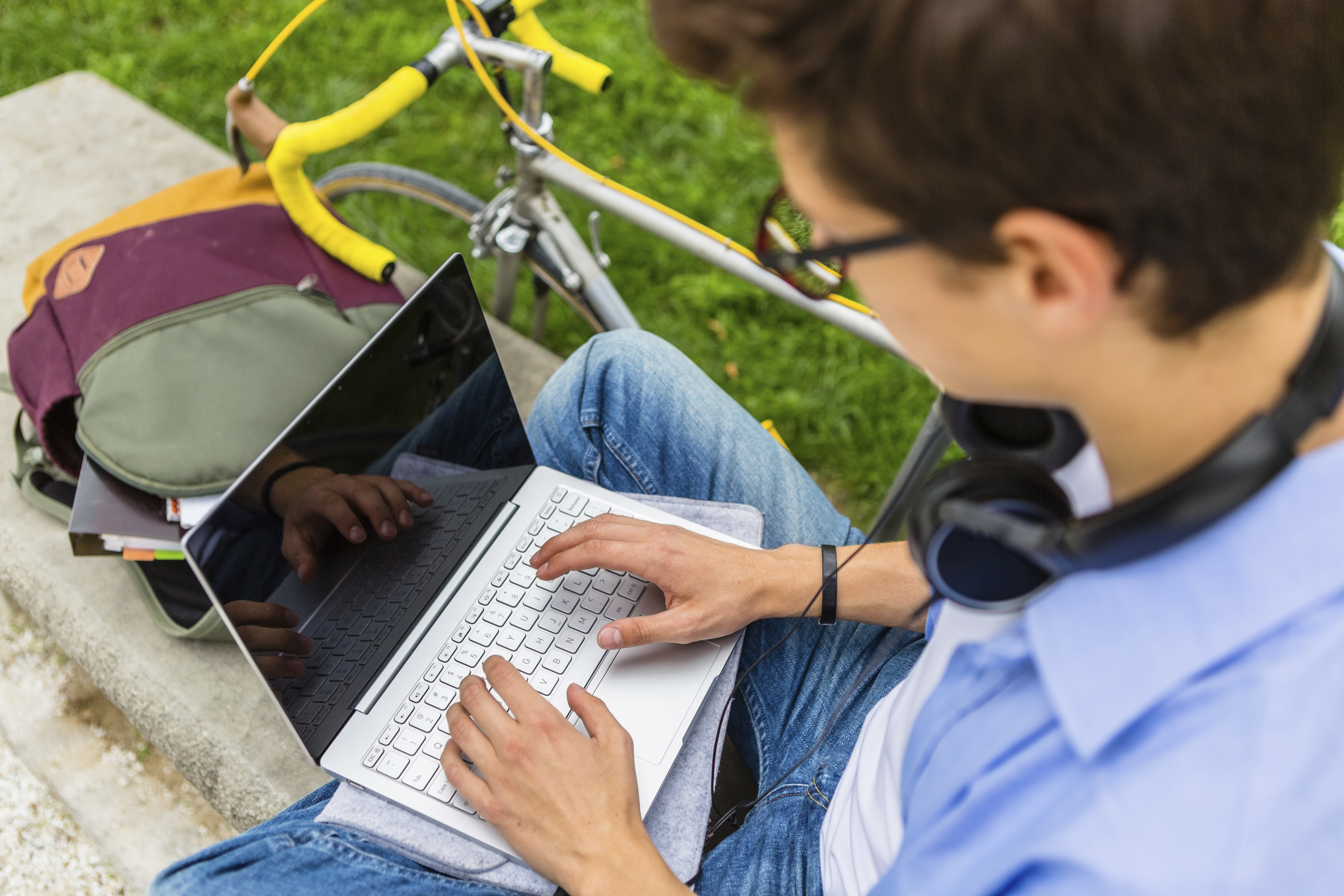 Overhead view of a male student wearing glasses and headphones using a laptop outside, emphasising digital well-being and safeguarding in online education.