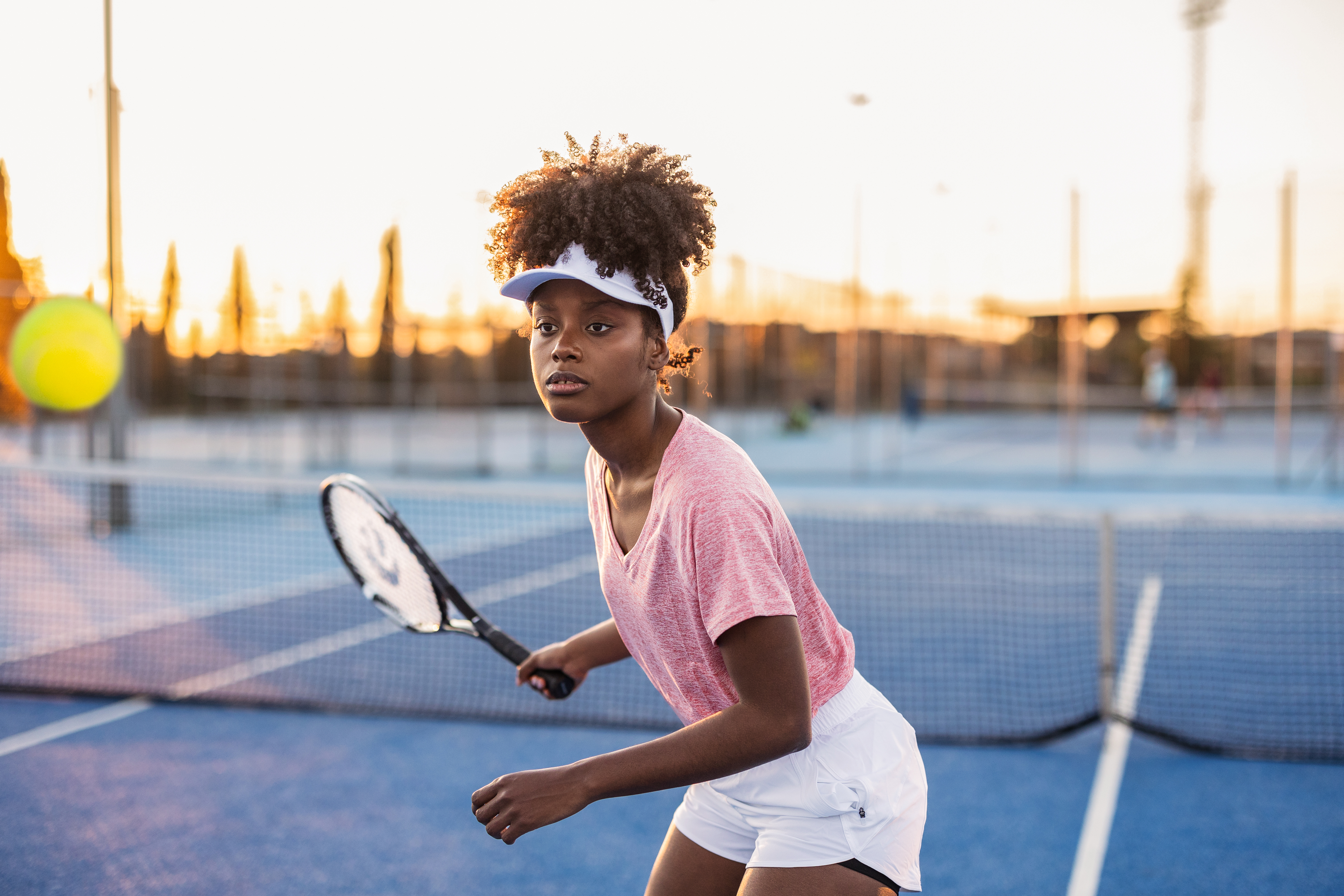 Focused young female tennis player on a blue court preparing to hit a ball. This image represents the dedication of elite student-athletes who rely on Pamoja Education's flexible online curriculum to balance rigorous training schedules with academic excellence.