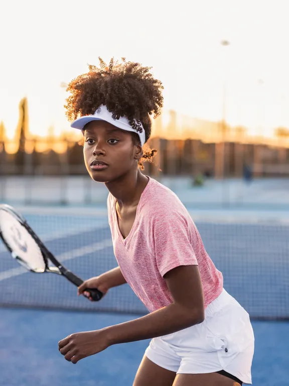 Focused young female tennis player on a blue court preparing to hit a ball. This image represents the dedication of elite student-athletes who rely on Pamoja Education's flexible online curriculum to balance rigorous training schedules with academic excellence.