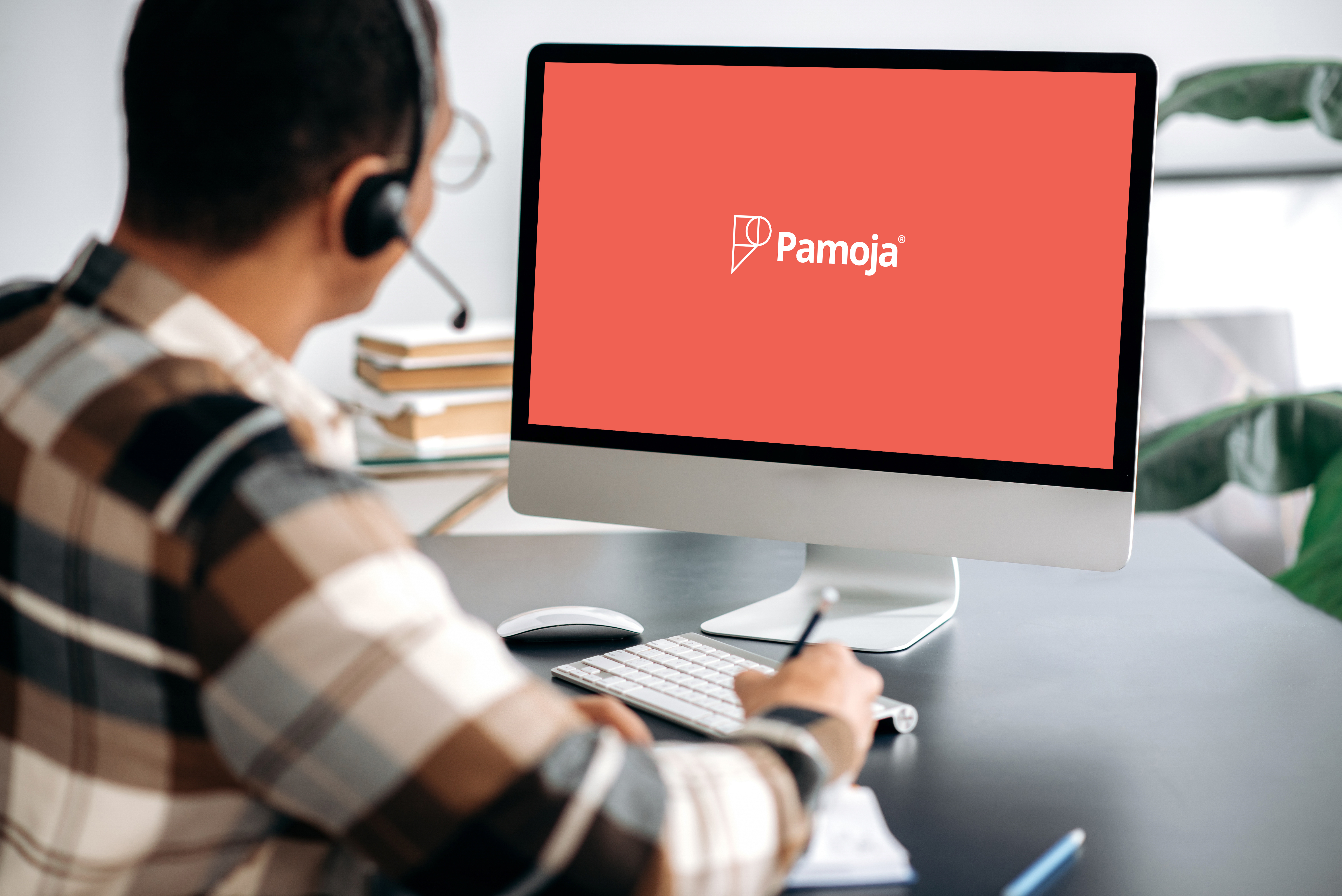 a person with a headset and a plaid shirt looking at a desktop monitor displaying the word 