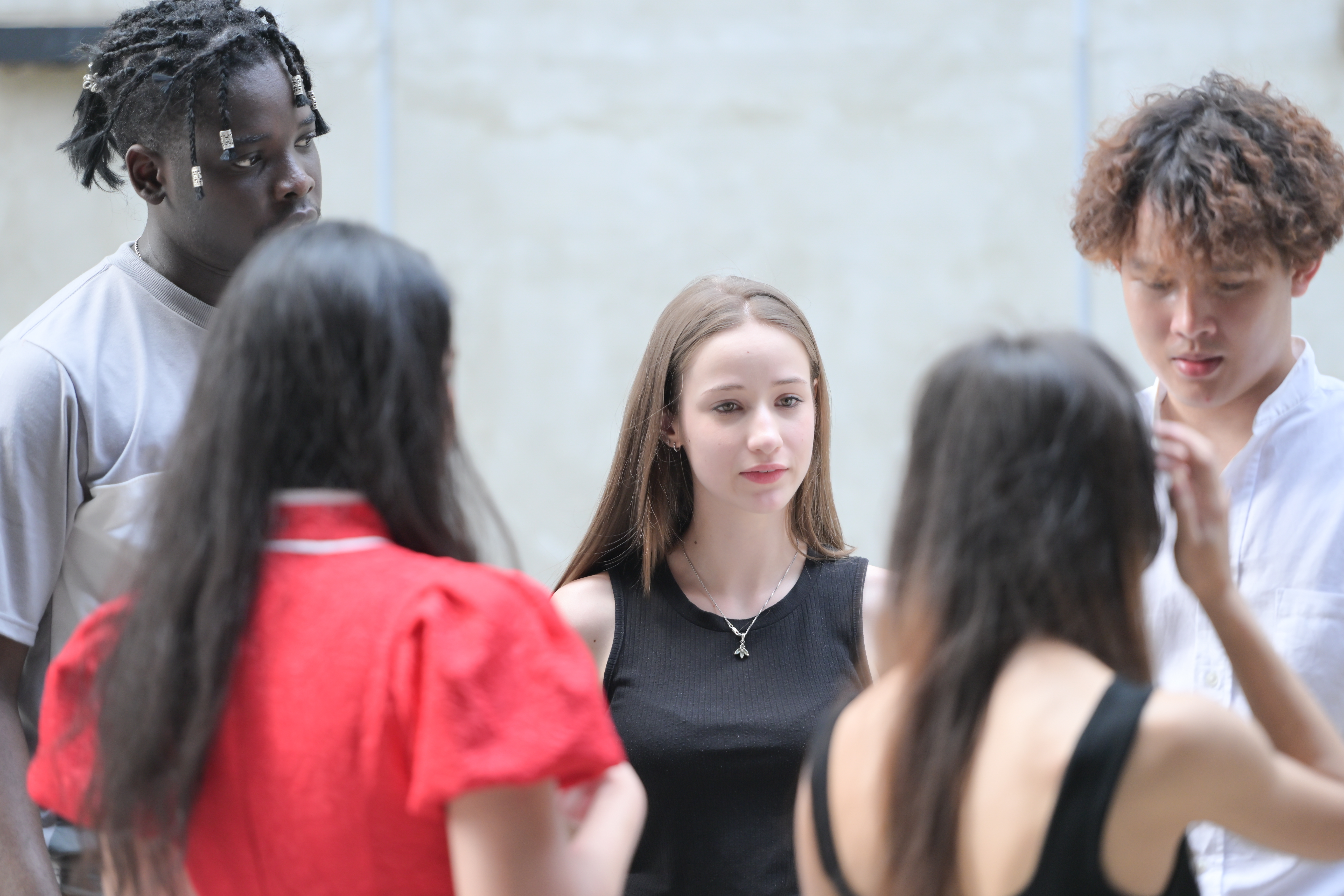 A diverse group of high school students standing in a circle, engaged in a focused discussion or conversation outdoors.
