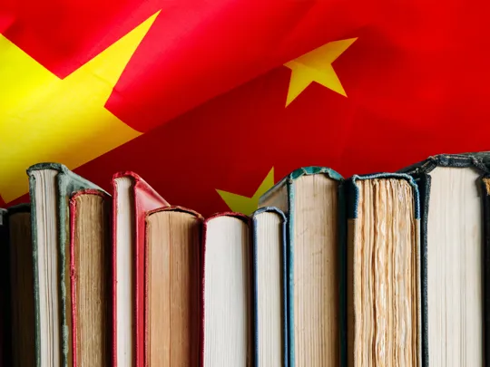 A close-up of a row of books against a vibrant red background of the Chinese flag with yellow stars, symbolizing Mandarin language study.