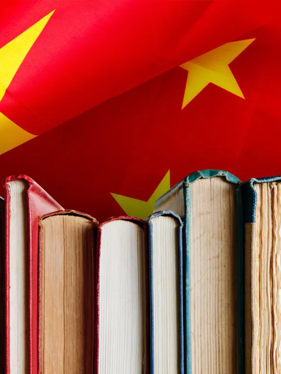 A close-up of a row of books against a vibrant red background of the Chinese flag with yellow stars, symbolizing Mandarin language study.
