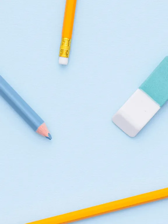A flat-lay image of various school supplies scattered on a light blue background. The supplies include yellow and colored pencils, a blue eraser, a ruler, and washi tape.