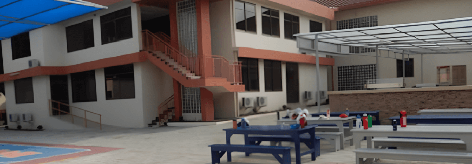 The courtyard of Lincoln Community School campus, featuring a two-story building with orange trim and outdoor seating area with blue and gray picnic tables.