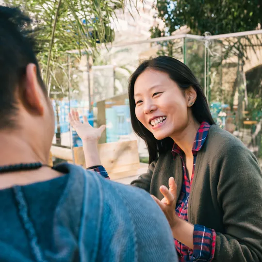 A young woman with long dark hair smiles while working on a laptop from the comfort of a couch, demonstrating the flexibility of online business management study.