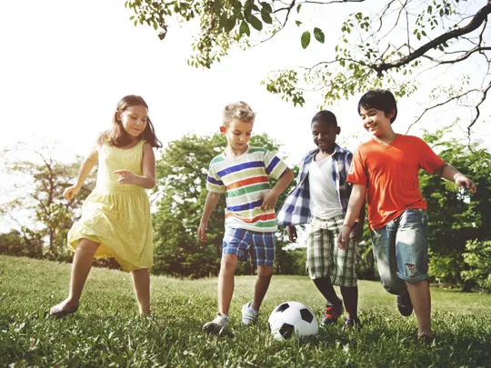 Group of young children running and kicking a football.