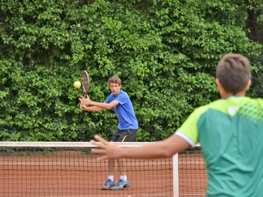 Two boys playing tennis together.