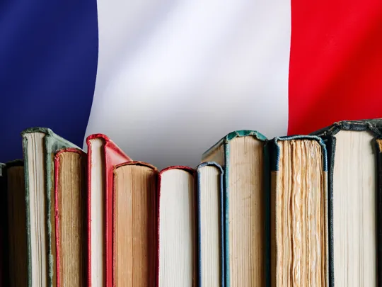 A close-up of a row of books against a background of the French flag, symbolizing the study of the French language and culture.