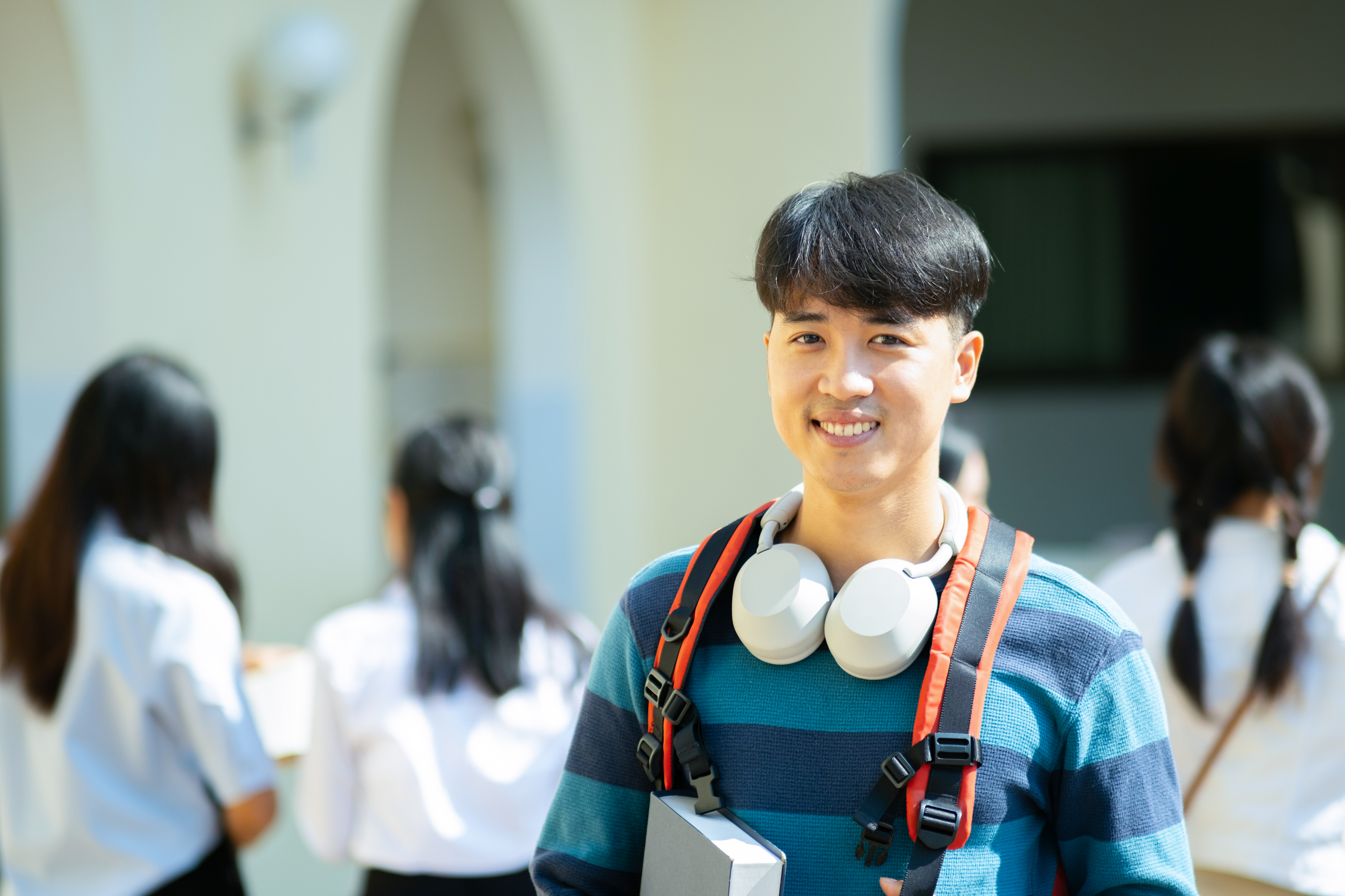Smiling gifted student with headphones and a backpack on a modern campus, representing engagement in advanced academic programs. This image symbolises Pamoja Education's ability to provide challenging IB courses and flexible online learning opportunities for exceptionally talented and gifted students.