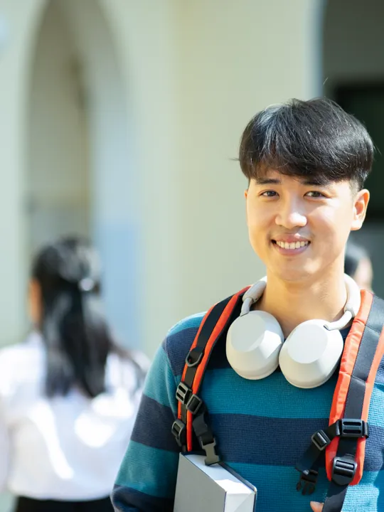Smiling gifted student with headphones and a backpack on a modern campus, representing engagement in advanced academic programs. This image symbolises Pamoja Education's ability to provide challenging IB courses and flexible online learning opportunities for exceptionally talented and gifted students.
