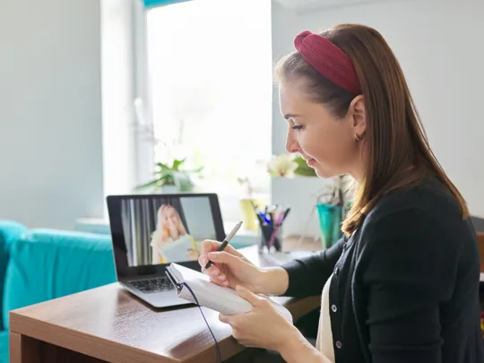 A woman watching a live Pamoja webinar, taking notes