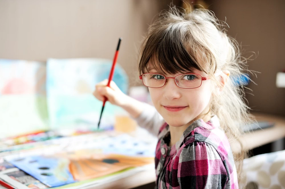 Female child smiling at the camera whilst painting. 