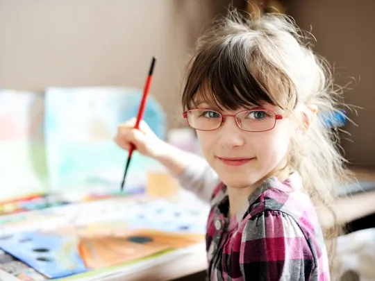 Female child smiling at the camera whilst painting.
