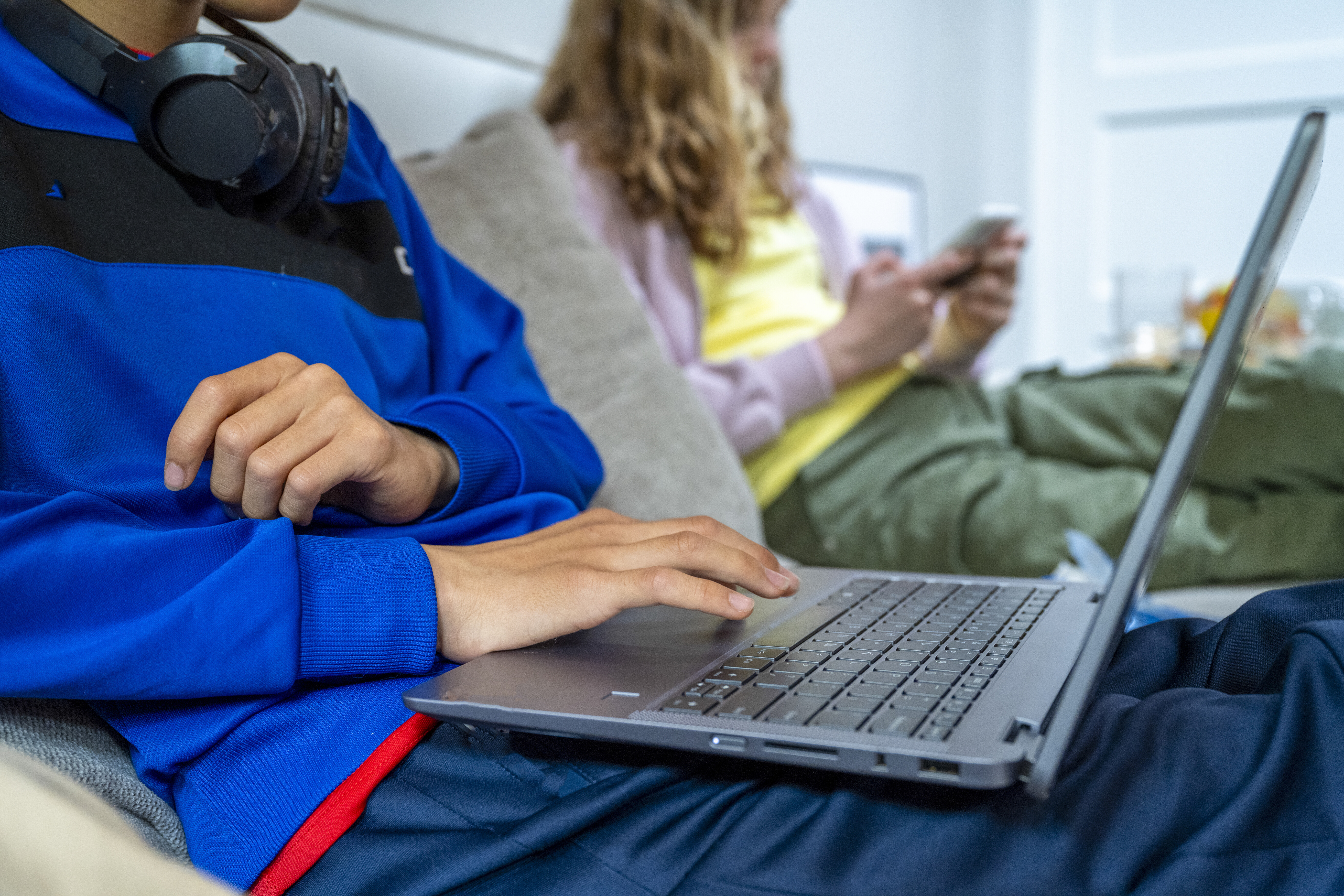 Close-up of a student using a laptop with headphones around their neck, representing responsible digital learning and online safety at Pamoja.