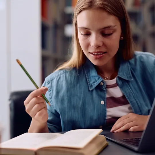 Focused young student studying with a book and laptop. This image emphasises concentration and personalised learning support for students with SEND (Special Educational Needs and Disabilities).