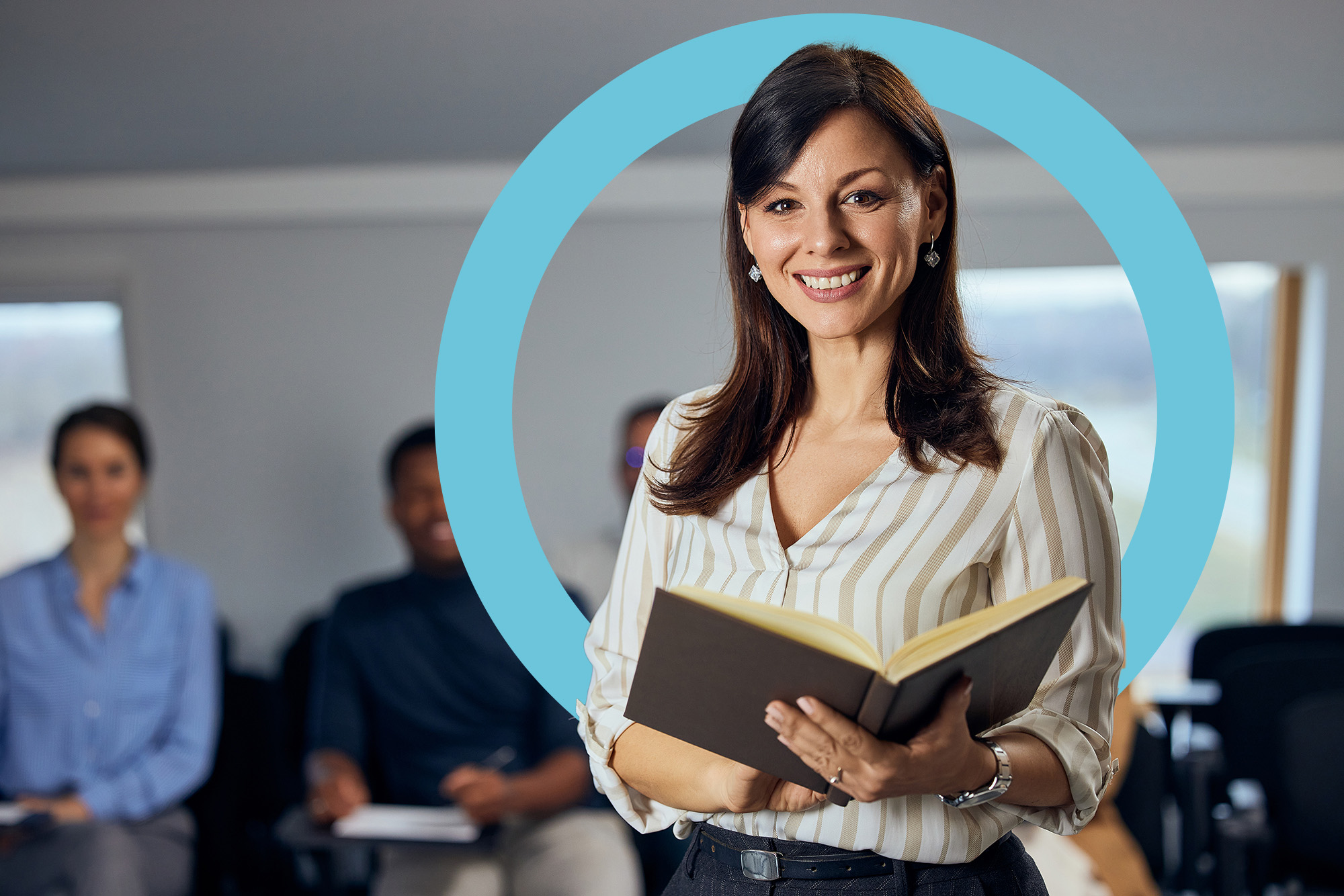 A teacher standing with a notebook, looking at the camera.