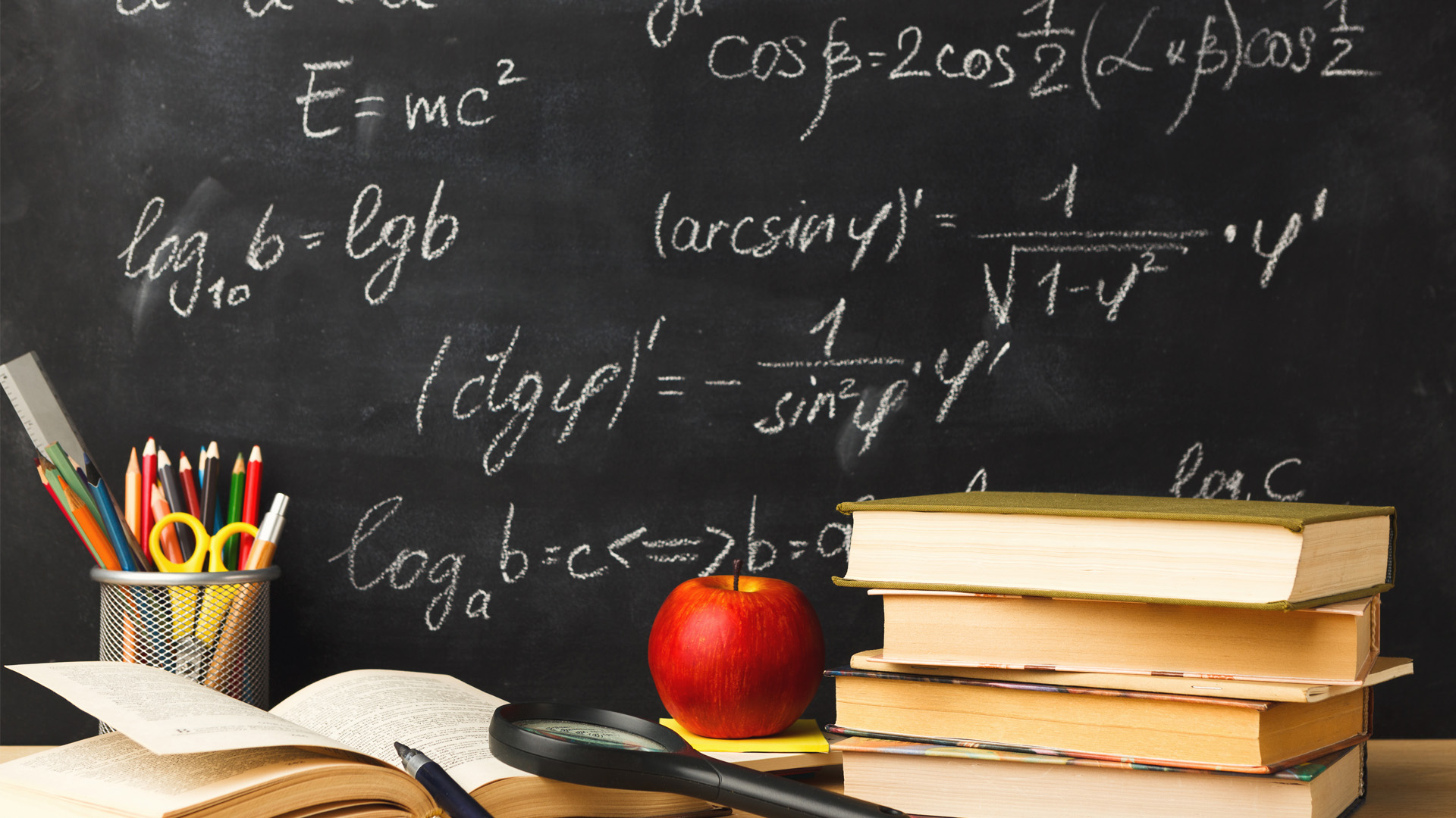 Close-up of a math classroom scene featuring a blackboard covered in complex mathematical equations, including trigonometry and logarithms. In the foreground, there's an open book, a stack of textbooks, a red apple, a magnifying glass, and a pencil holder filled with colorful pens and pencils.