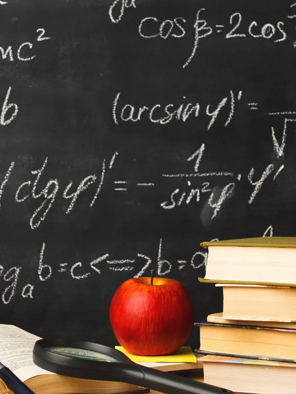 Close-up of a math classroom scene featuring a blackboard covered in complex mathematical equations, including trigonometry and logarithms. In the foreground, there's an open book, a stack of textbooks, a red apple, a magnifying glass, and a pencil holder filled with colorful pens and pencils.