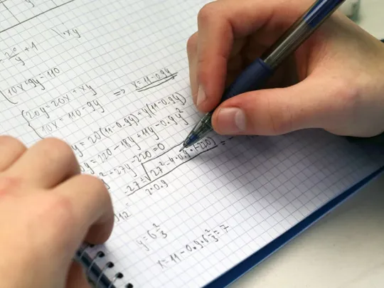 A student completing maths sums in a maths workbook.