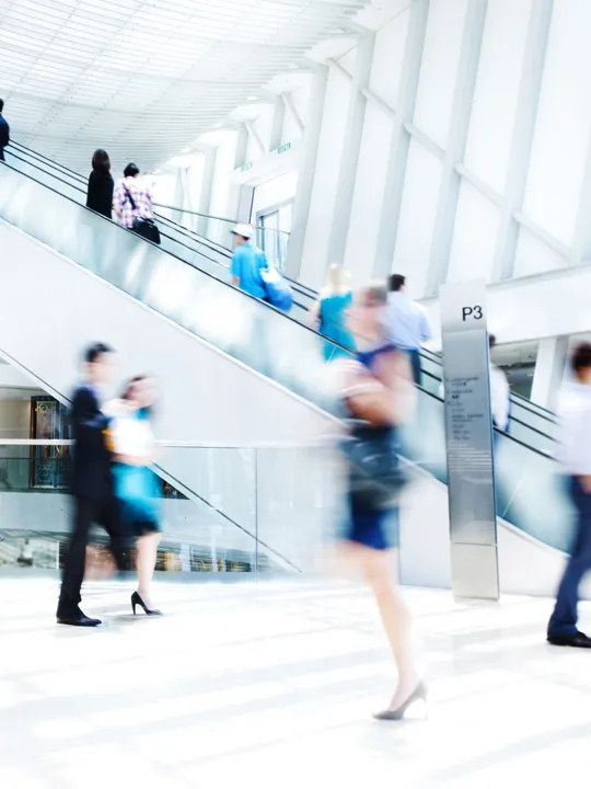 A young woman in a plaid shirt smiles and gestures enthusiastically while talking to a person in an outdoor cafe setting about business management.