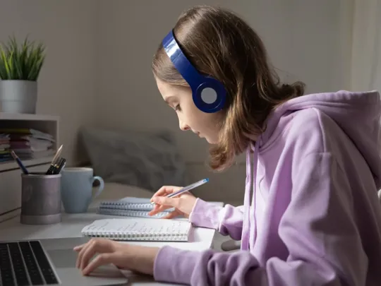 Teen student studying at desk wearing headphones.